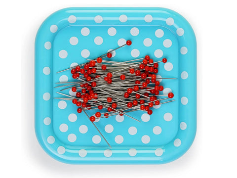 A blue polka dot magnetic pin cushion holds a pile of red glass head pins.