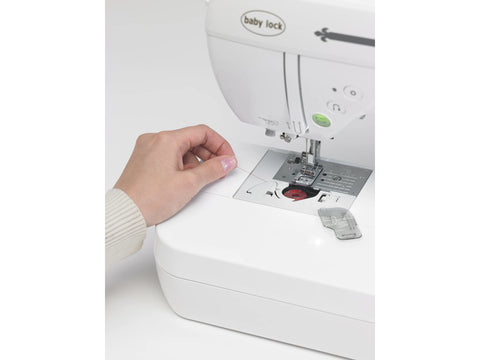 A person's hand threads a white Baby Lock Presto II sewing machine.