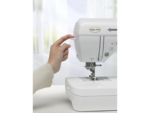 A hand adjusts a white Baby Lock Presto II sewing and quilting machine.