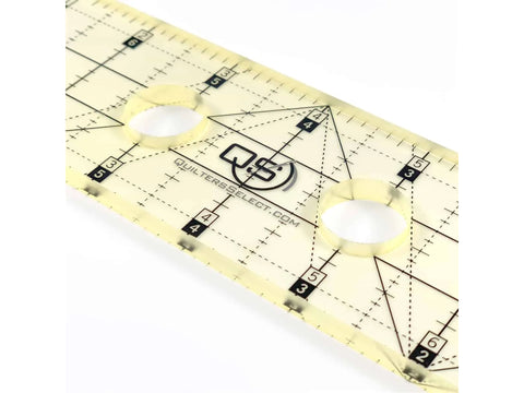 A clear, non-slip quilting ruler with black markings and two circular finger holes.