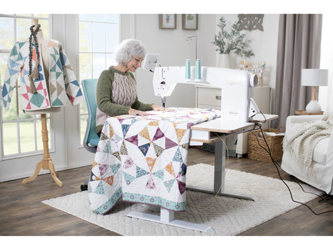 A woman quilts on a white Baby Lock Regalia stationary machine with a lift table.