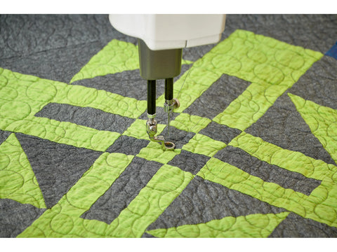 A close-up of a sewing machine needle quilting a green and gray patterned fabric.