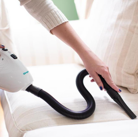 A person uses a Simplicity Flash handheld vacuum to clean a couch.