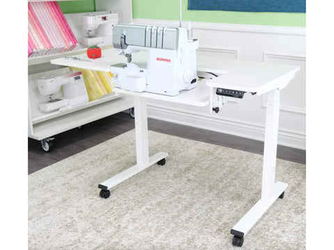 White electric height-adjustable sewing and cutting table with a Bernina serger.