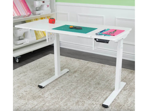 A white electric height-adjustable sewing and cutting table with crafting tools on top.