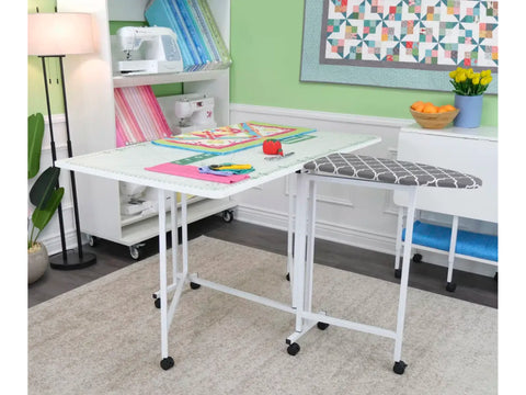 White folding cutting and ironing table with wheels in a craft room.