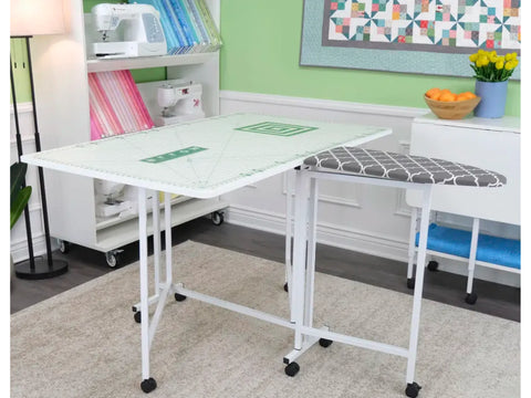 A white cutting and ironing table with a green grid mat and a gray patterned ironing board.