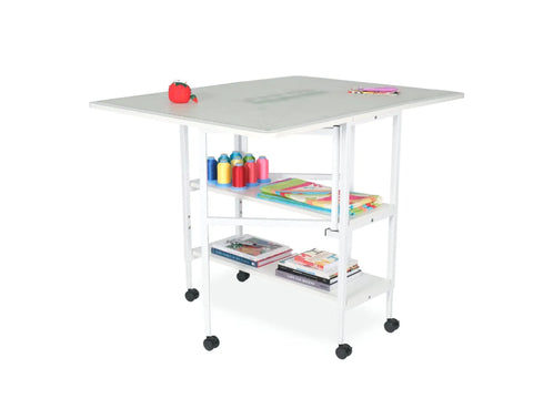 A white Arrow Dixie Cutting Table with sewing supplies and books on its shelves.