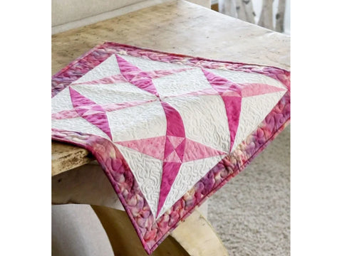 A pink and white quilted table runner with a star pattern rests on a wooden table.