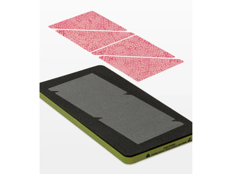 A cutting die with a green base and black foam, shown with pink fabric cut into triangles.