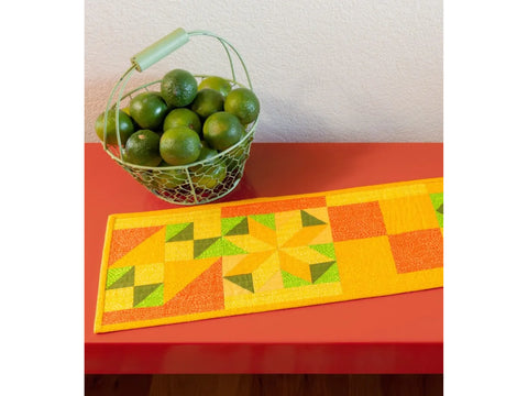 A wire basket of limes sits next to a colorful quilted table runner.