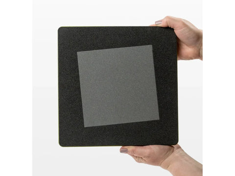 A person holds a black square AccuQuilt GO! die with a 6-1/2 inch square blade.