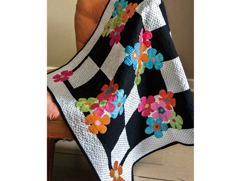 A black and white polka dot quilt with colorful floral appliques is draped over a chair.