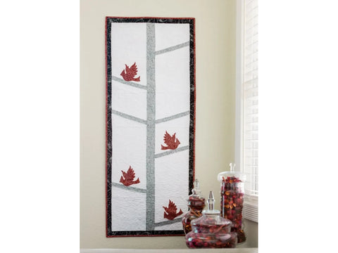 A quilted wall hanging with red birds on tree branches, next to glass jars of potpourri.