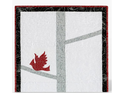 A quilted wall hanging features a red cardinal on a gray tree branch against a white background.