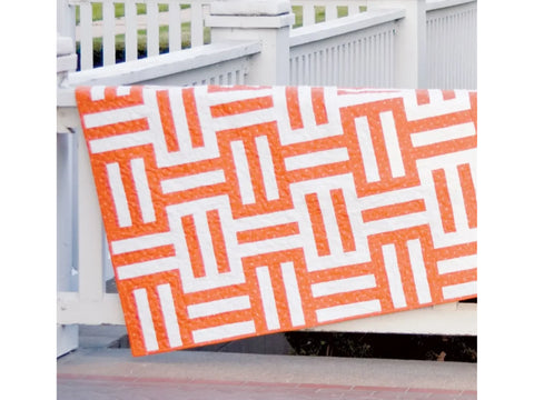 An orange and white patterned quilt hangs over a white railing.