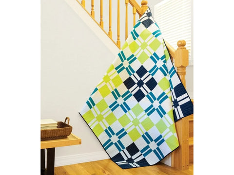 A colorful quilt with a geometric pattern of squares and rectangles hangs over a wooden staircase.