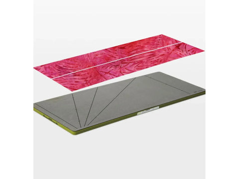 A pink patterned fabric strip lies above a gray AccuQuilt GO! strip cutter.