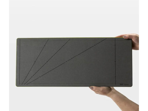 A person holds a dark gray AccuQuilt GO! strip cutter with measurement markings.