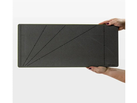 A person holds a dark gray AccuQuilt GO! Strip Cutter with measurement markings.