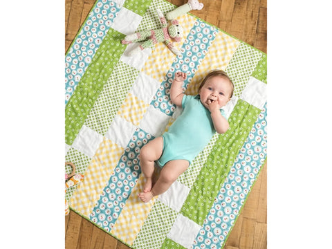 A baby lies on a colorful patchwork quilt with various patterns and colors.