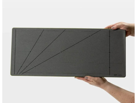 A gray cutting mat with angled guidelines is held by two hands.