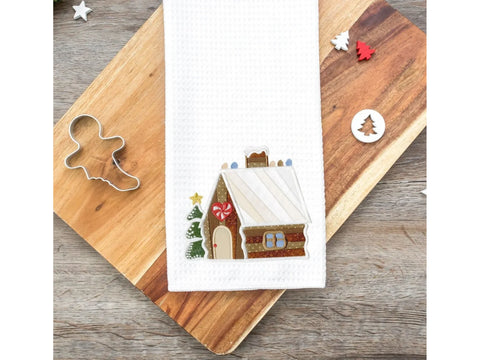 White waffle weave towel with an embroidered gingerbread house and Christmas tree.