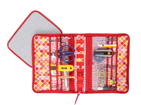 A red fabric tool case with a colorful patterned interior, filled with various sewing and crafting tools.