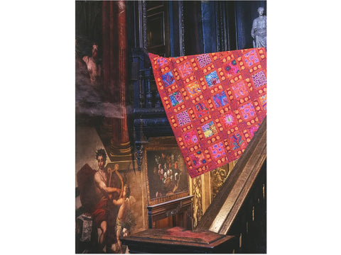 A vibrant red patterned quilt draped over a dark wooden railing in a castle setting.
