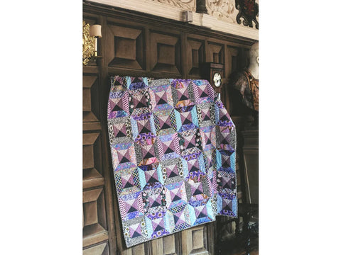 A colorful Kaffe Fassett quilt with geometric patterns hangs on a dark wood-paneled wall.
