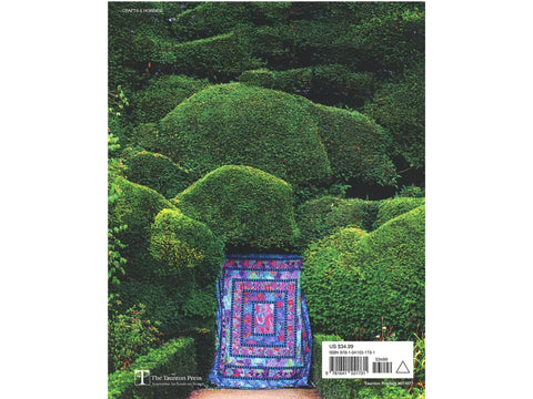 A colorful quilt hangs in a lush green garden with sculpted hedges.