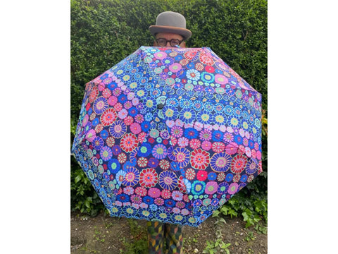 Kaffe Fassett Umbrella in magenta with a floral pattern, held by a person in a bowler hat.