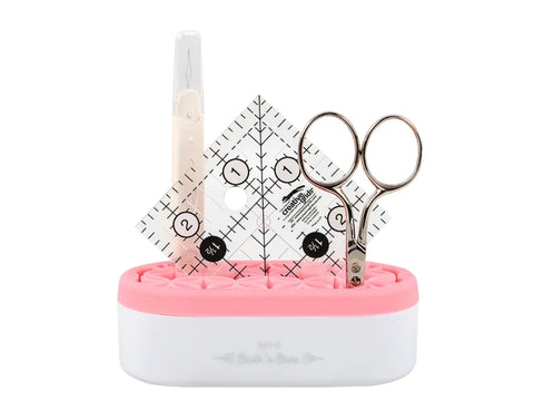 A pink and white mini organizer holds a seam ripper, two clear rulers, and a pair of scissors.