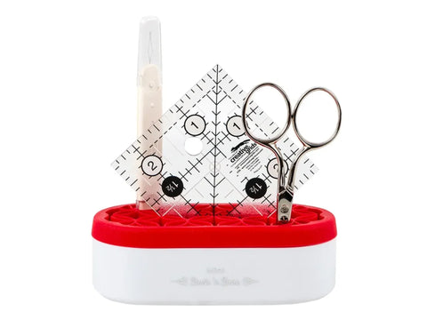 A red and white mini organizer holds a seam ripper, ruler, and small scissors.