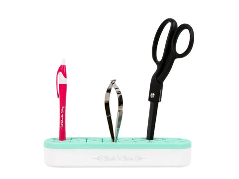 A mint and white Stash 'n Store organizer holds a pink pen, silver tweezers, and black scissors.