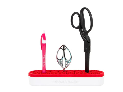 A red and white Stash N' Store organizer holds a pink pen, decorative scissors, and black scissors.