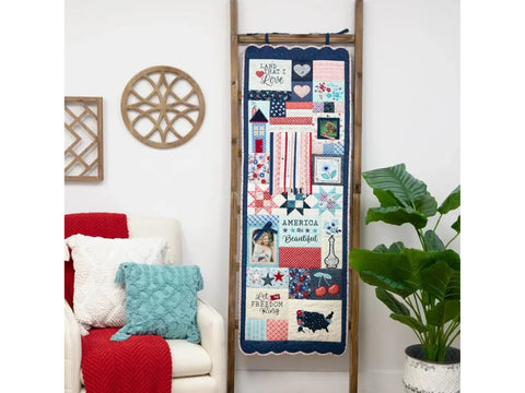 A patriotic quilt with various Americana-themed blocks hangs on a wooden ladder.