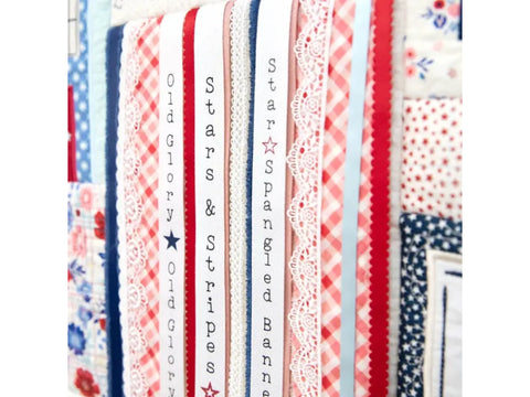 A close-up of patriotic ribbons and fabrics, some with text like "Old Glory" and "Stars & Stripes."