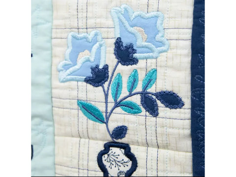 A close-up of a quilted fabric with blue floral embroidery in a vase.