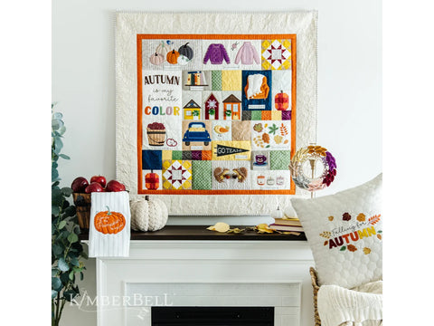 A quilted wall hanging with various autumn-themed embroidered squares, displayed above a fireplace.