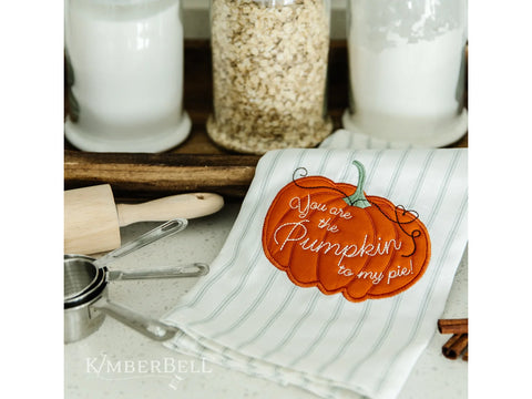 A white and gray striped kitchen towel with an embroidered orange pumpkin that says, "You are the pumpkin to my pie!"