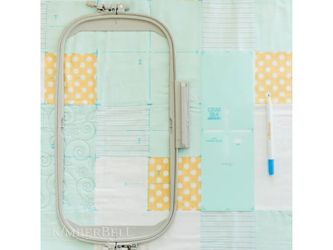 An embroidery hoop, a blue ruler, and a blue marker are on a quilt.