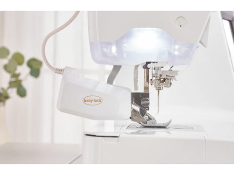 A white Baby Lock Ballad sewing and quilting machine with an illuminated needle area.