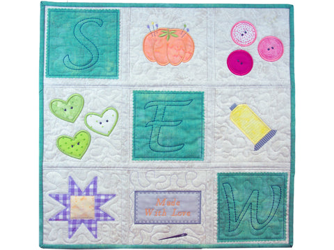 A quilted wall hanging features sewing-themed blocks and spells out "SEW."
