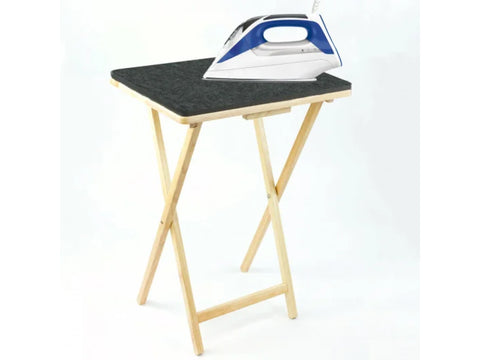 A blue and white iron rests on a dark gray wool pressing mat atop a wooden folding table.