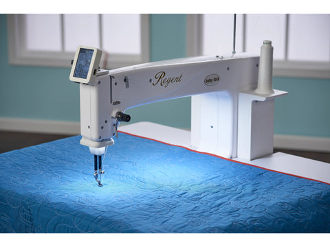 A white Baby Lock Regent 18" sit-down quilting machine is actively quilting a blue fabric.