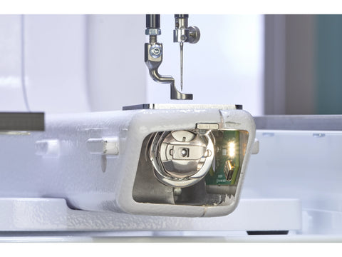 A close-up of a sewing machine's needle and bobbin area with an illuminated circuit board.