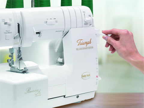 A white Baby Lock Triumph serger with a hand adjusting a lever on the right side.