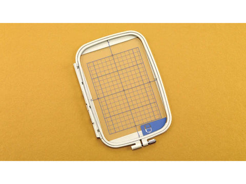 A white 5x7 embroidery frame with a blue grid on a yellow background.