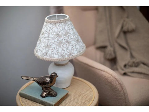 A white lamp with an embroidered shade sits on a table next to a bronze bird figurine.